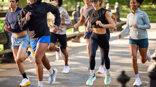 Runner lacing a cushioned trainer for an easy day while a lightweight workout shoe and recovery slides sit nearby on the track.
