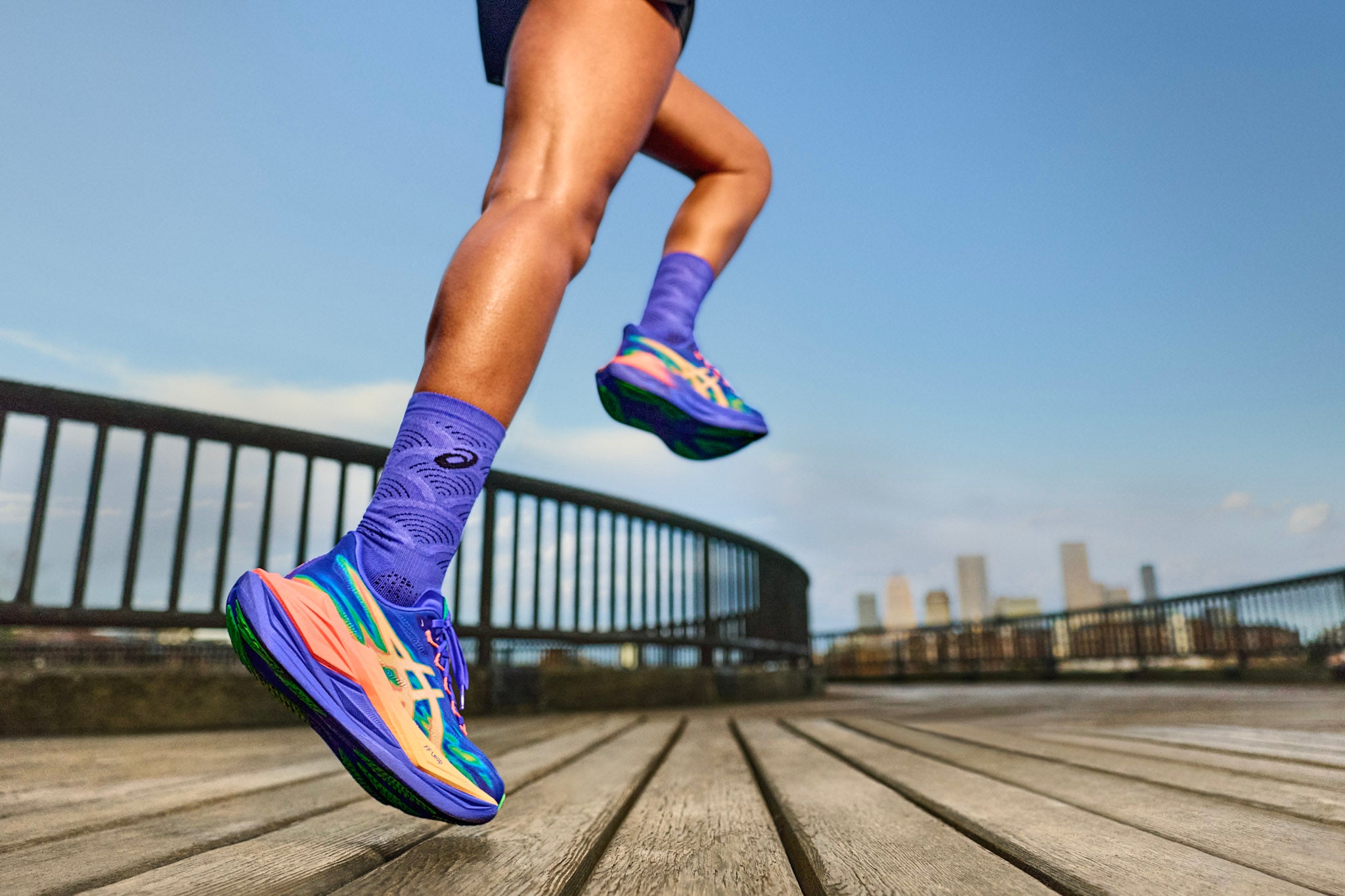 Runner striding on a sunlit road with shoes showing curved rocker and moderate heel-to-toe drop, illustrating smooth forward roll.