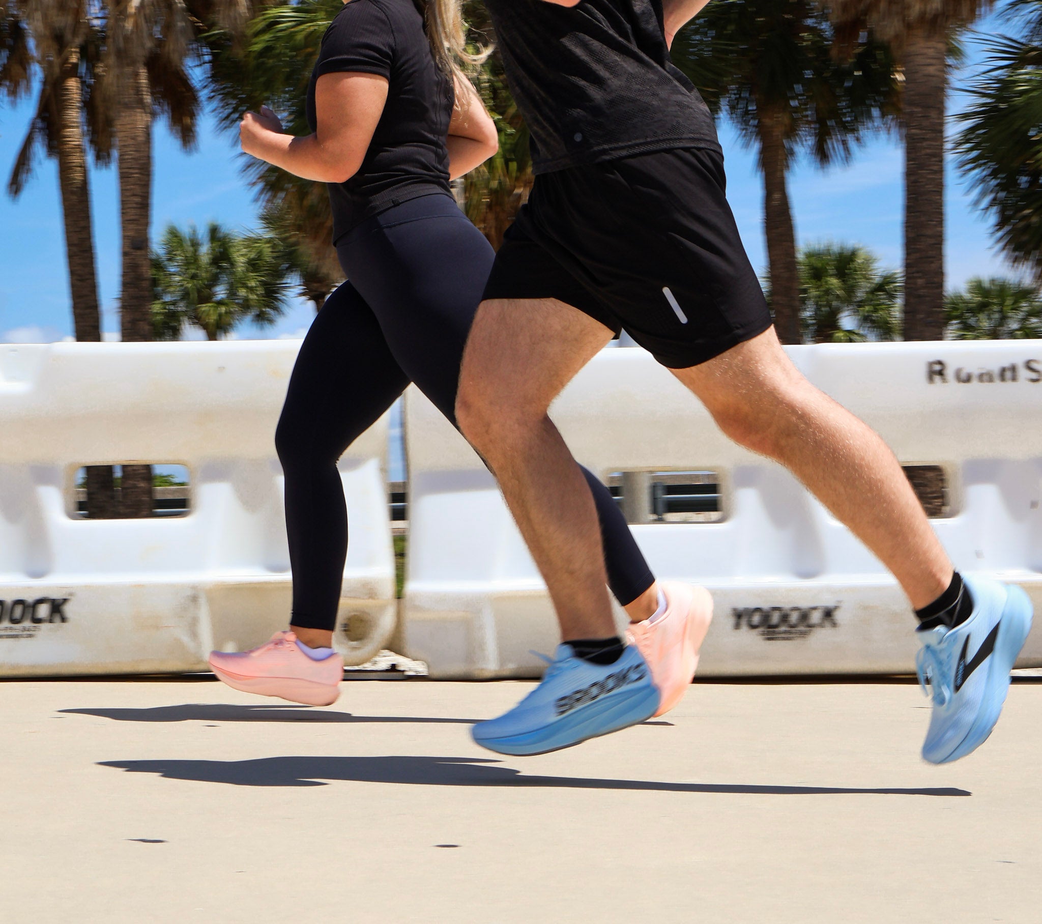 Close-up of a runner pressing a thumb at the front of a shoe to check toe room while comparing two different last shapes on a fitting bench.