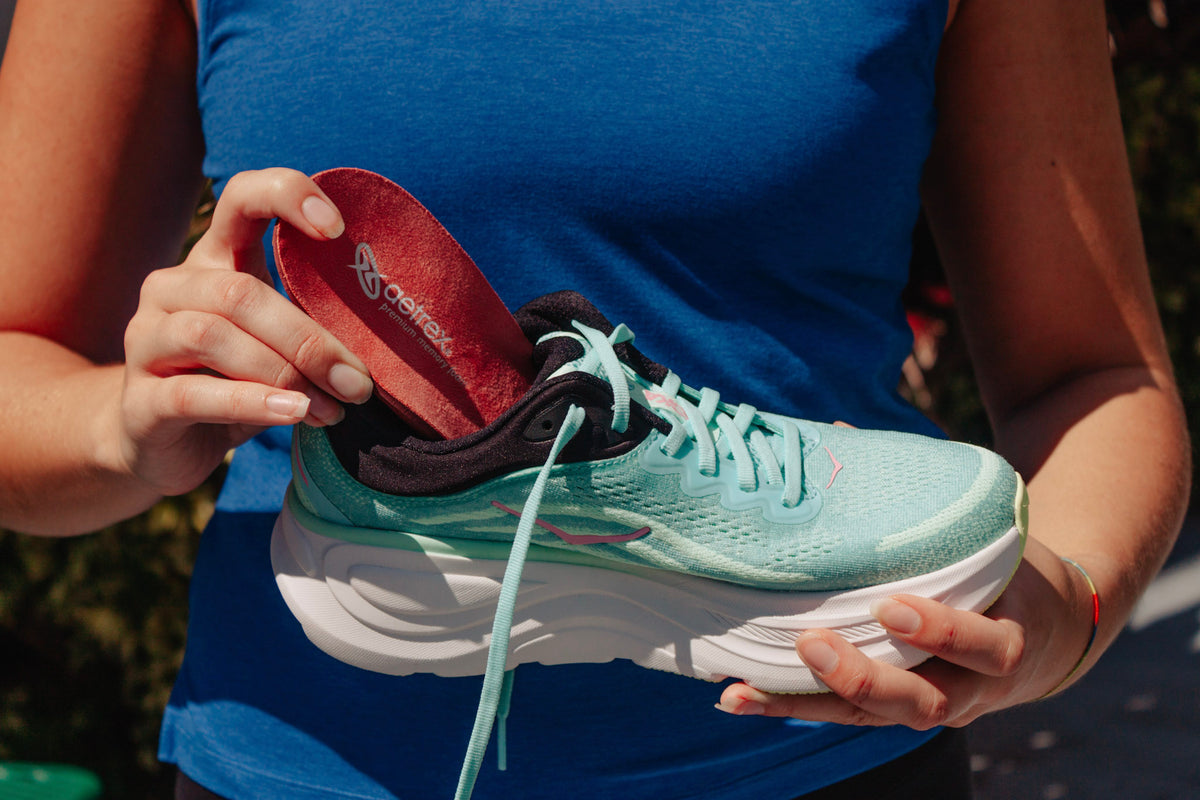 Close-up of a runner swapping a new orthotic into a trainer while the stock liner sits beside it.