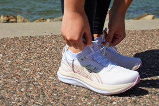 Runner lacing a breathable mesh road shoe with supportive overlays and a padded collar, sunlight highlighting airflow through the upper.