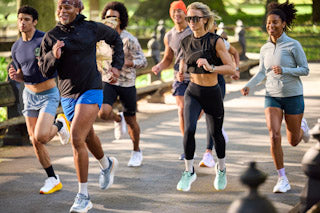 Runner lacing a cushioned trainer for an easy day while a lightweight workout shoe and recovery slides sit nearby on the track.