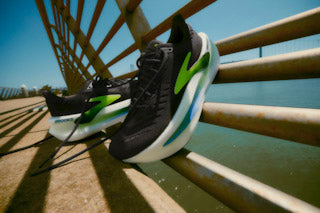 Runner striding on a paved path wearing rockered road shoes; a dashed line illustrates heel-to-toe drop and the upturned toe spring.