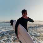 Surfer carrying a surfboard while checking a Garmin smartwatch