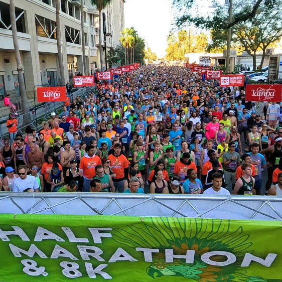 Large crowd of participants at a half marathon and 8K event with banners and logos.