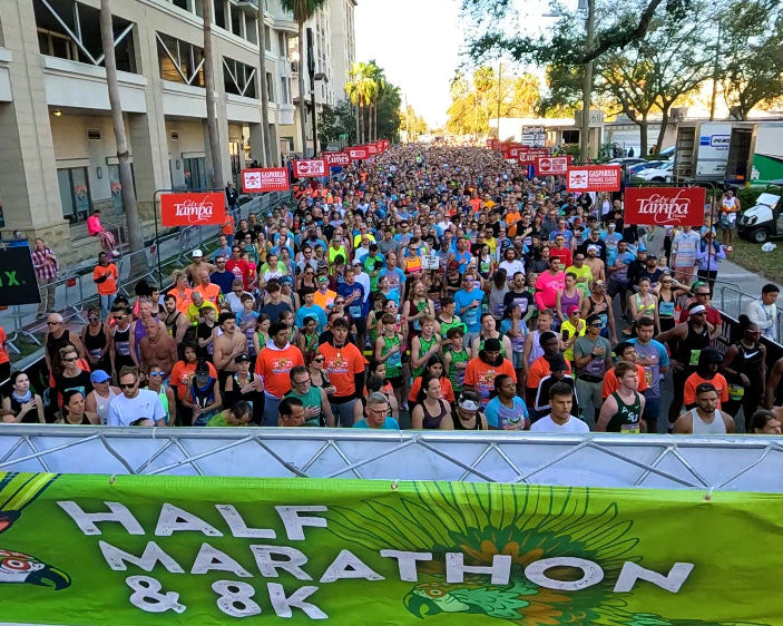 Large crowd of participants at a half marathon and 8K event with banners and logos.